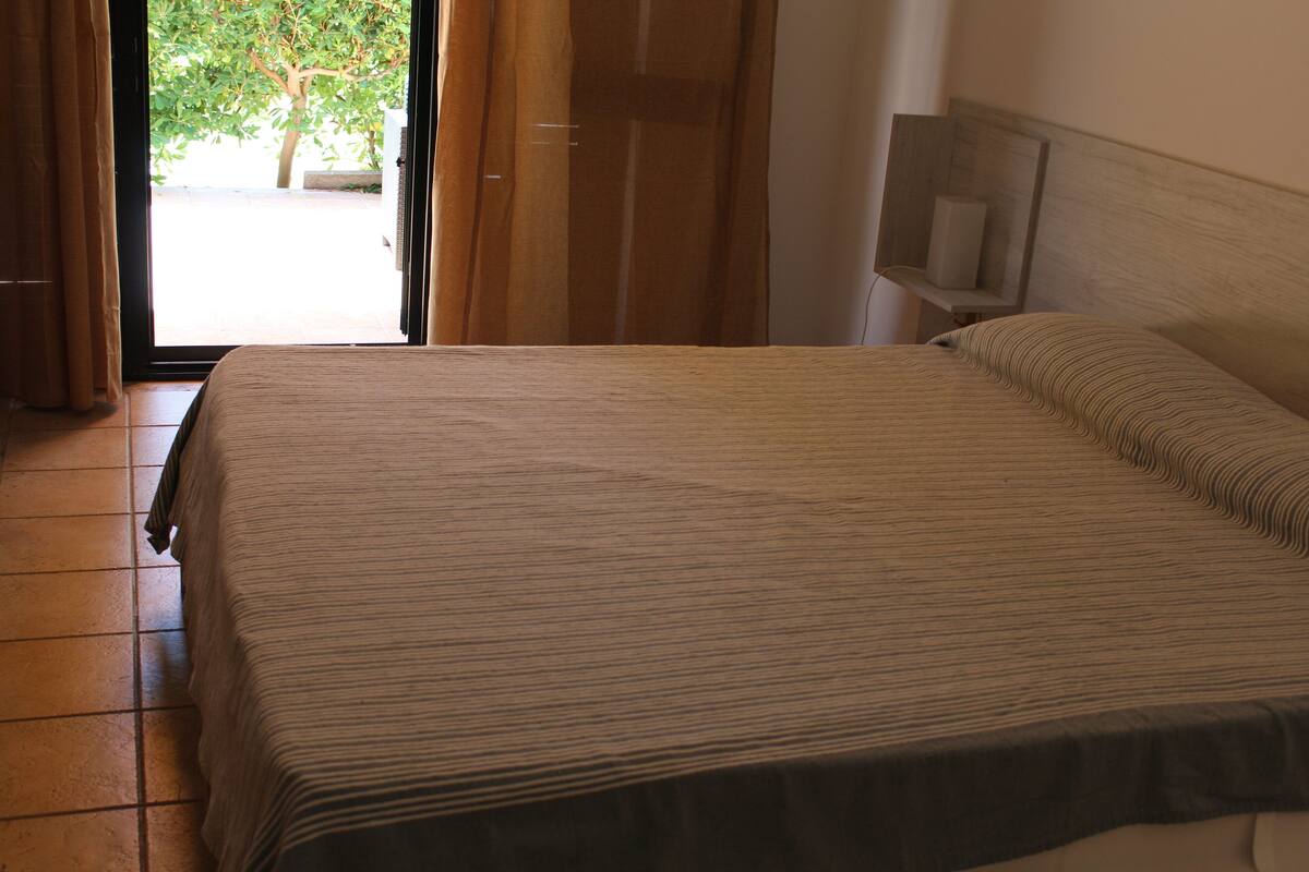 Una camera d'albergo con un letto, una televisione su un mobile in legno e una porta che dà su uno spazio esterno con un albero.