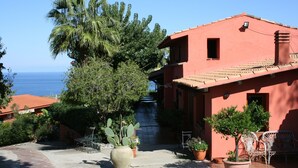 Un edificio rojo con tejado de tejas, rodeado de plantas en macetas y mobiliario de exterior.