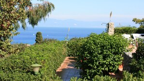 Un sendero en un jardín que lleva a una construcción de piedra con vistas al mar.