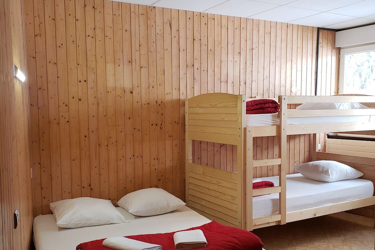 A room with a bunk bed and a single bed, wooden walls, a tiled ceiling, and a window.
