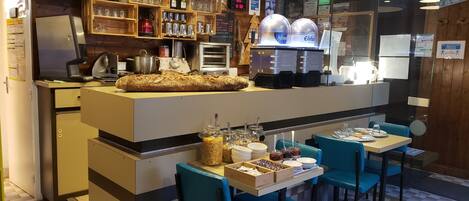Een restaurant met een centrale toonbank, blauwe stoelen en diverse glazen en flessen op planken.