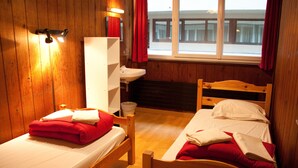 Una habitación de madera con dos camas, un lavamanos y una ventana con cortinas.