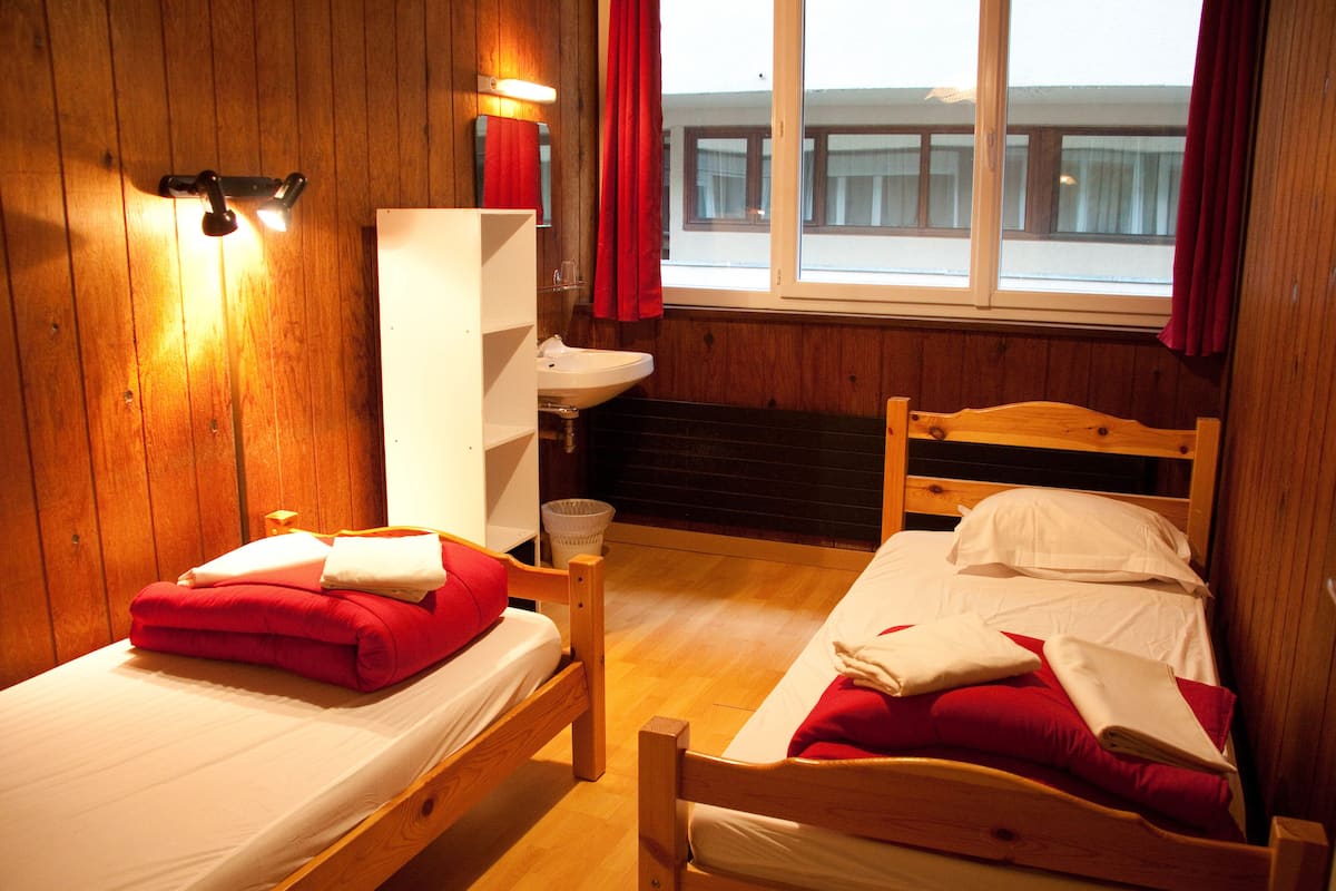 A wooden room with two beds, a sink, and a window with curtains.