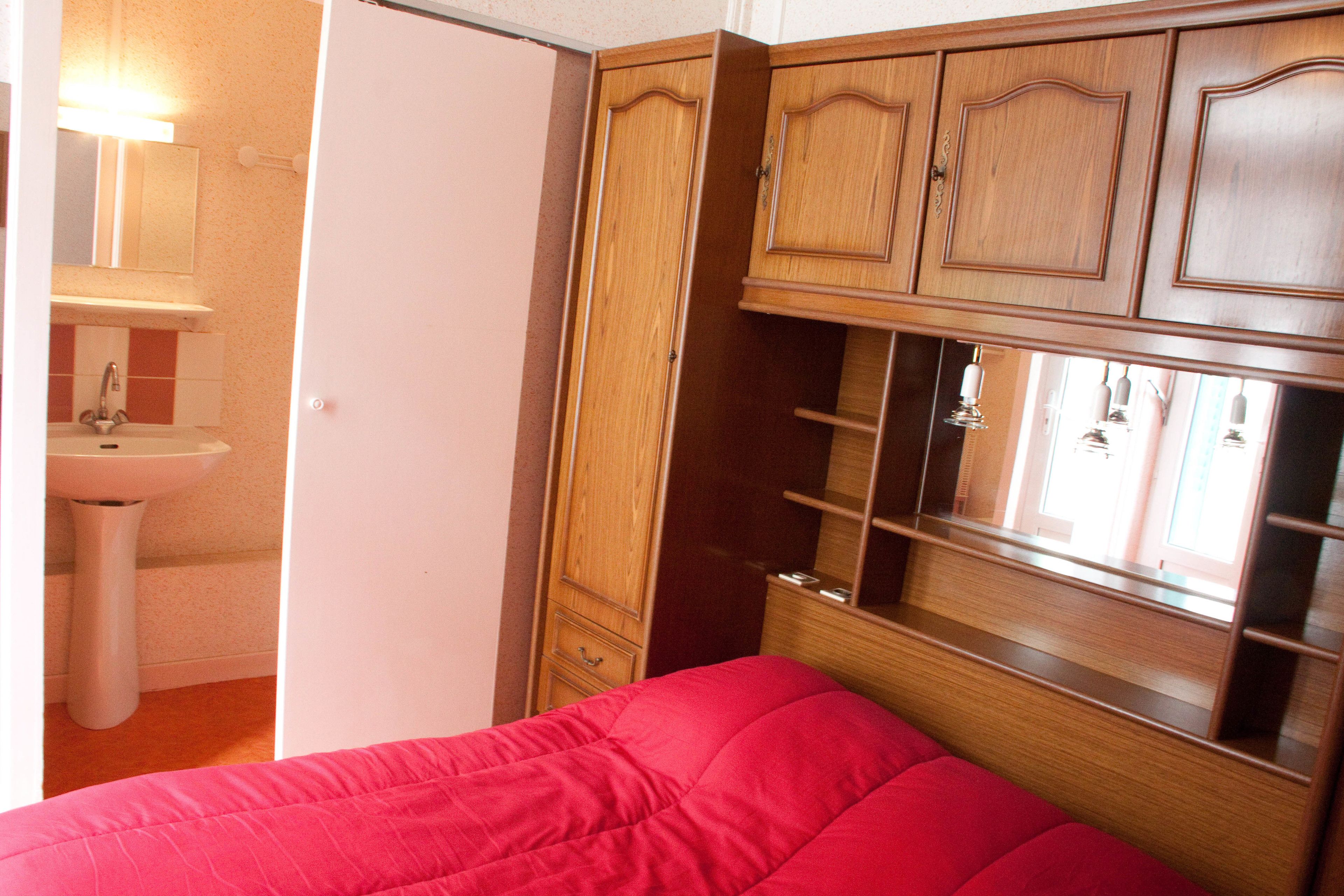 A bedroom with a wooden wardrobe, a red bed, and a white sink.