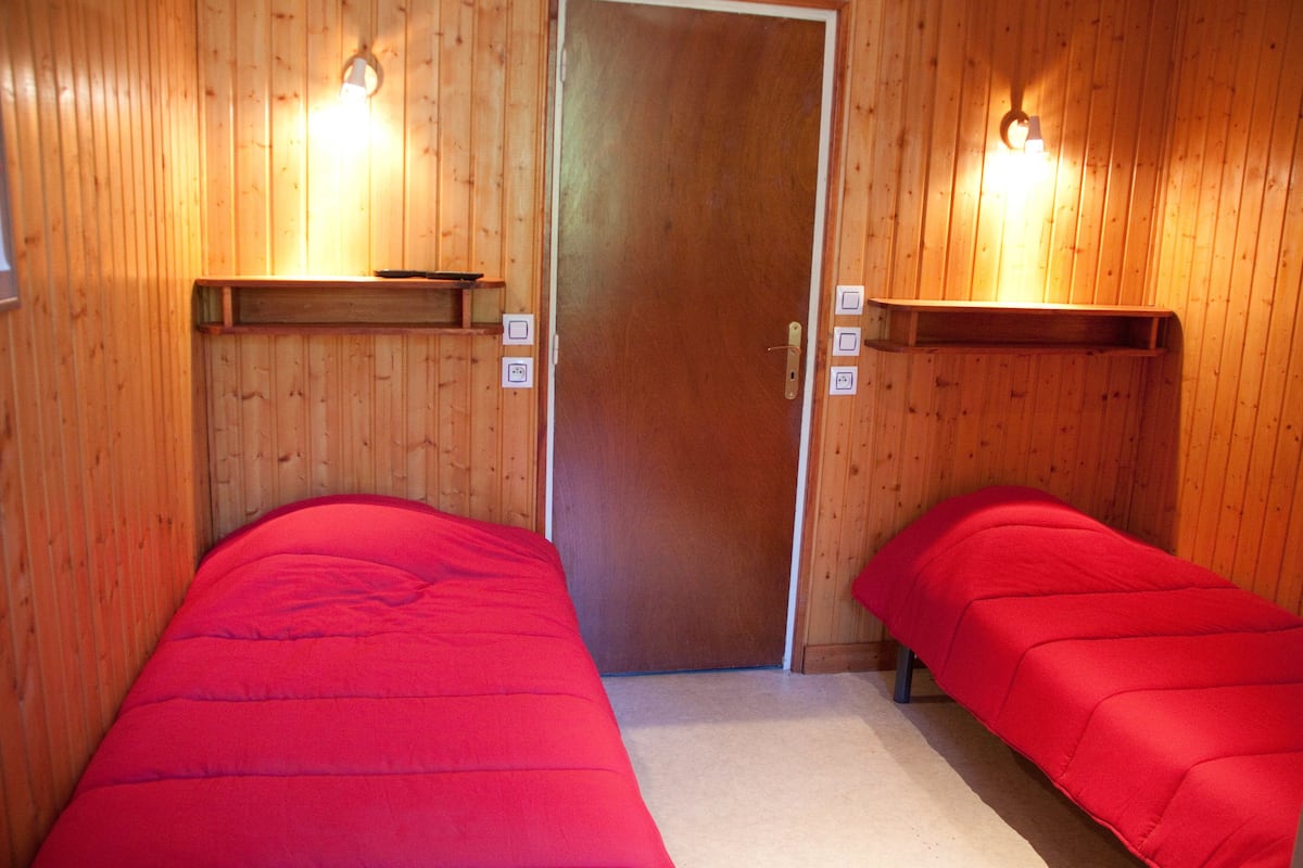 A room with two beds, wooden walls, and built-in shelves.