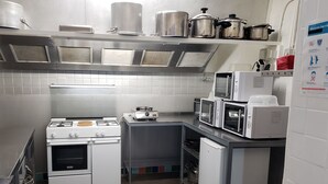Cocina industrial con electrodomésticos de acero inoxidable, incluyendo estufa, hornos y microondas, un salpicadero de azulejos y una campana extractora metálica.