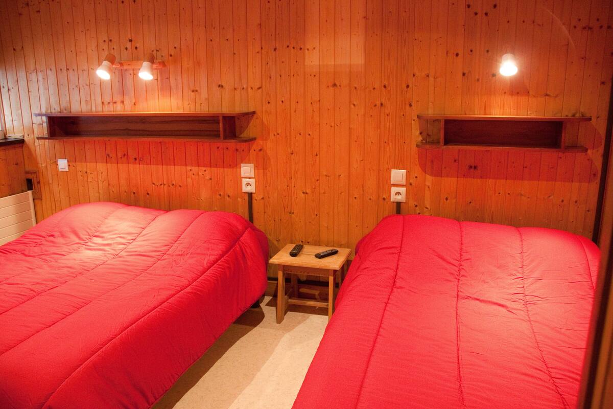 A room with two beds, wooden walls, and a small table with two remote controls.