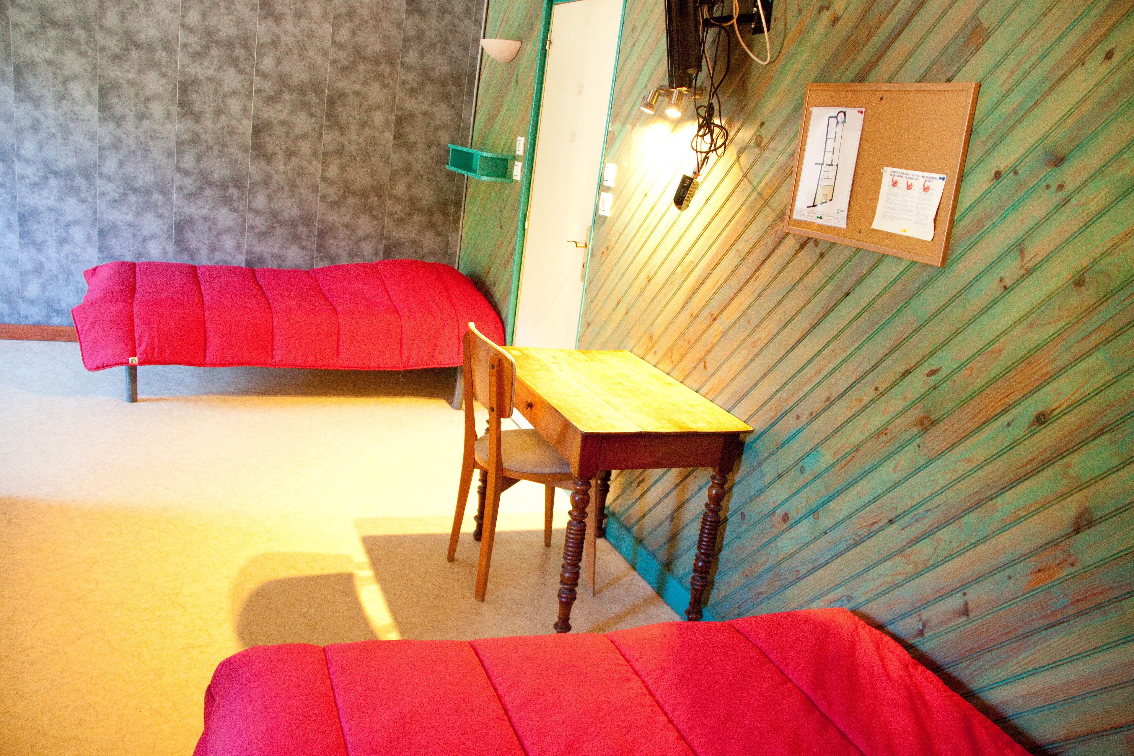 Une pièce avec un bureau en bois, une chaise rouge et un canapé rouge. Un tableau d’affichage avec des papiers est accroché au mur.
