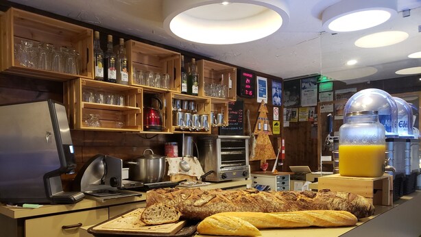 Un mostrador de panadería con pan, una máquina de café y un dispensador de zumo.