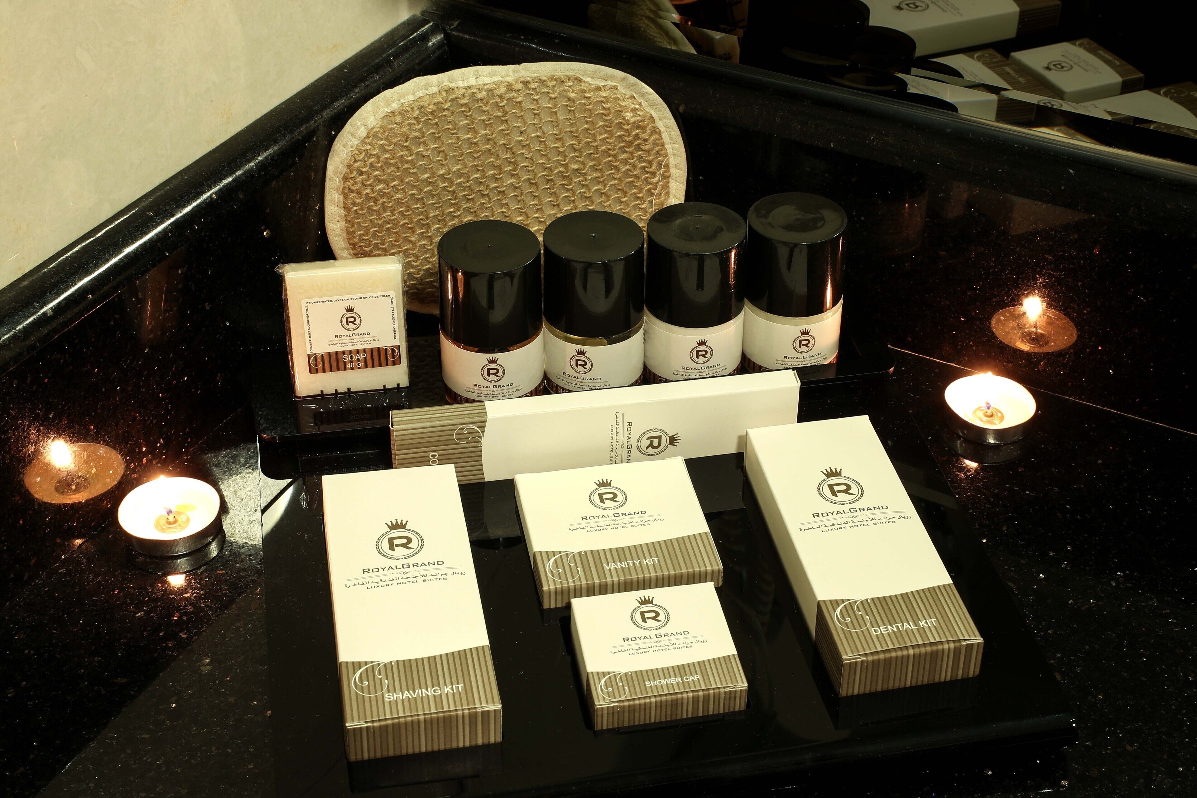Presentación de productos Royal Grand, incluyendo jabones, un kit de afeitado y un kit dental, sobre una encimera negra con velas.