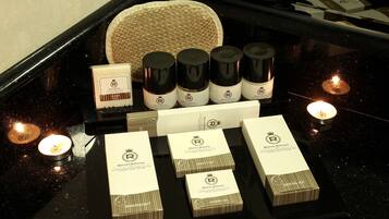 Presentación de productos Royal Grand, incluyendo jabones, un kit de afeitado y un kit dental, sobre una encimera negra con velas.