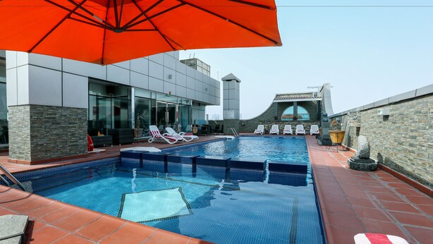 A rooftop swimming pool with clear blue water, surrounded by lounge chairs and a red umbrella.