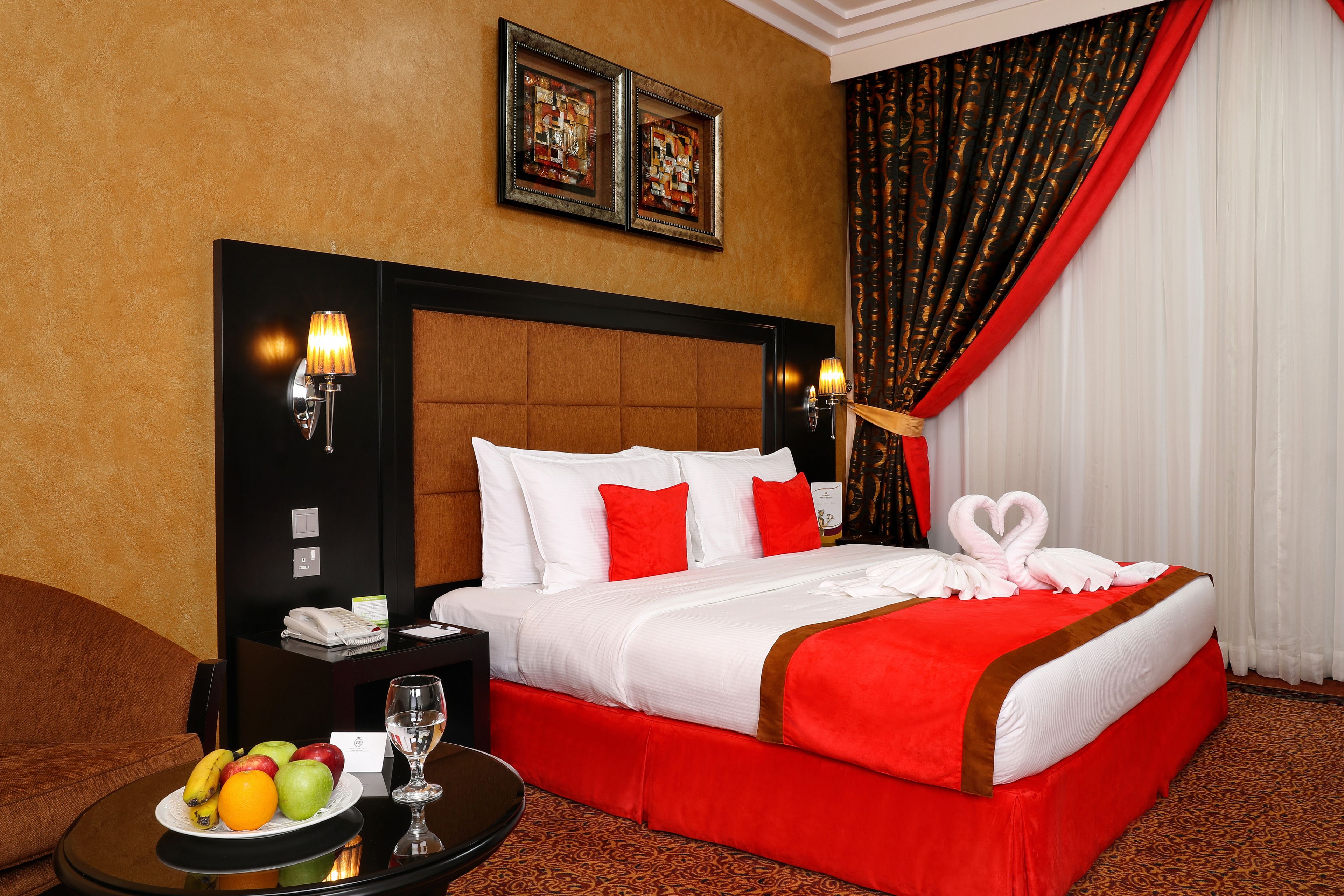 Een hotelkamer met een groot bed, een nachtkastje met een schaal fruit en een glas, en een hoofdeinde met wandlampen.