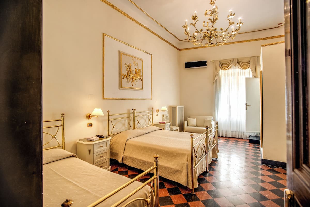 A hotel room with two beds, a chandelier, a framed picture on the wall, and a checkered floor.