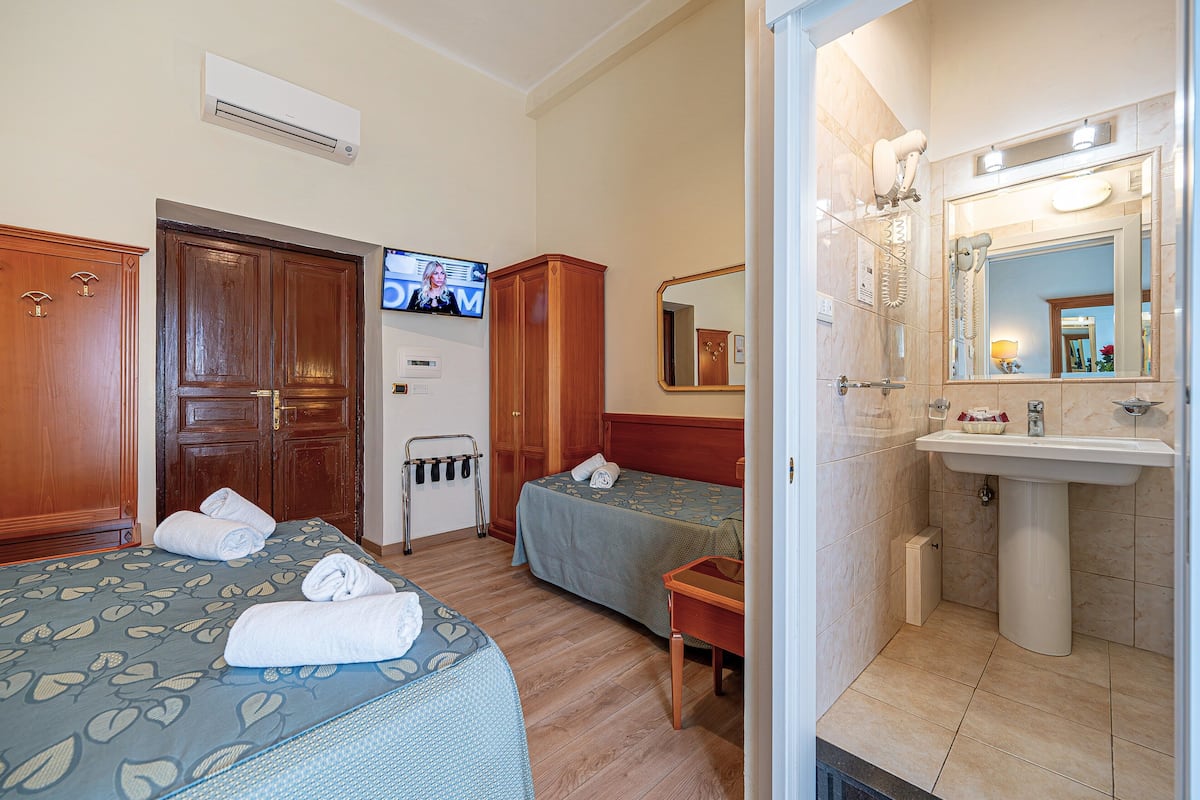 A hotel room with two beds, a TV, a bathroom with a sink, and a mirror.