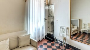 A hotel room with a sofa, a chair, a mirror, and a shower area. - Hotel Labelle  (Rome)