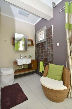 A bathroom with a white sink, mirror, and a wicker chair with cushions.