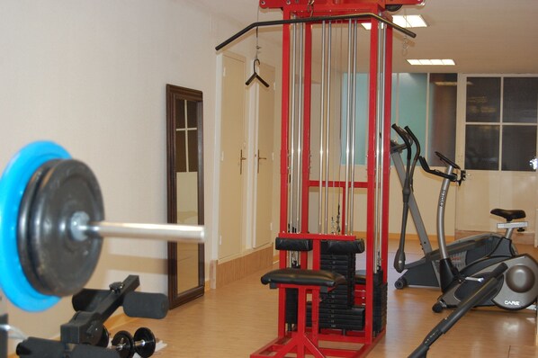 A gym with a barbell, weight plates, a bench press, and an exercise bike. - Hôtel de Compostelle (Sarlat-la-Canéda)