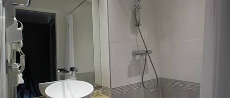 A modern bathroom with a large sink, a shower, and a mirror.