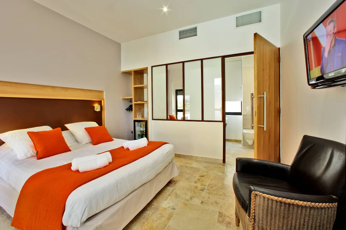 A hotel room with a large bed, a wooden headboard, a television, a wardrobe, and a wicker chair.