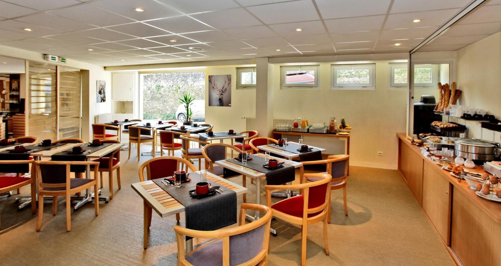 Un espace repas comprenant plusieurs tables et chaises, un buffet garni de différents plats et une grande fenêtre laissant entrer la lumière naturelle.