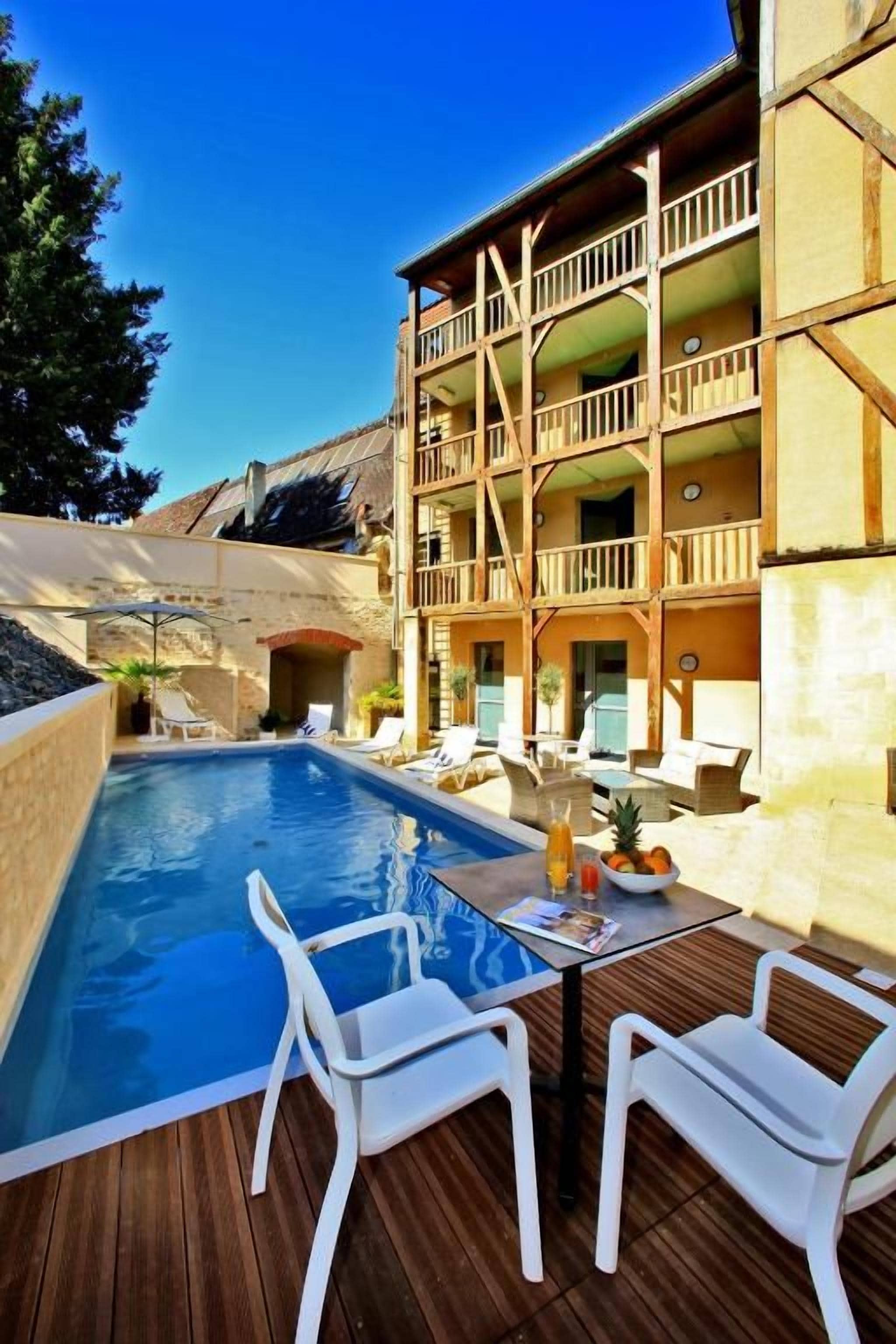 A poolside area with a table and chairs, a wooden deck, and a building with balconies.