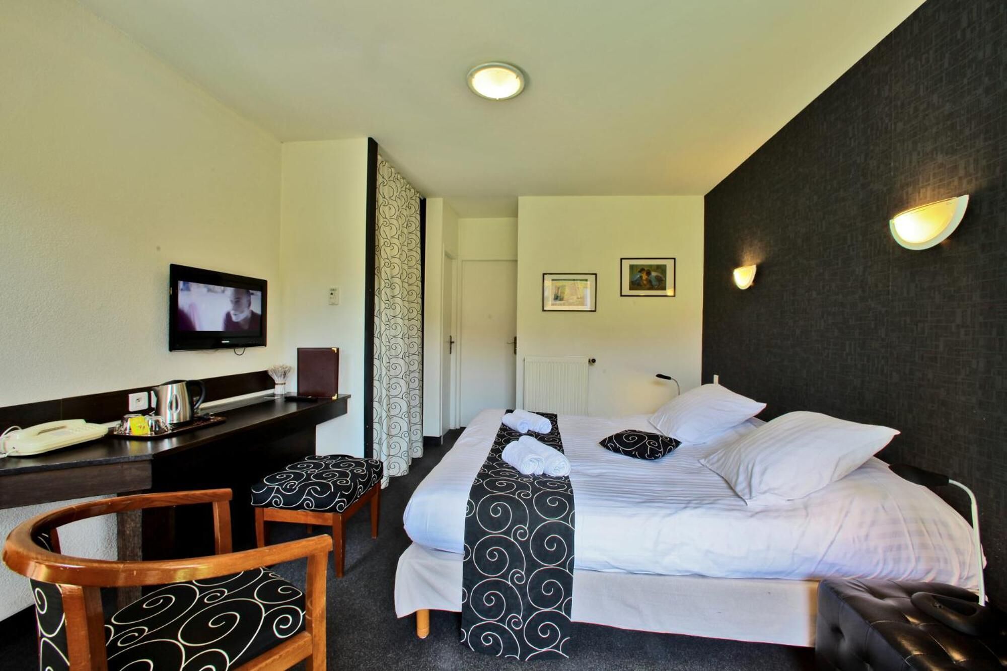 Una habitación de hotel con una cama, un escritorio con teléfono, televisión y una silla.