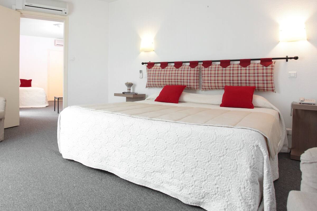 A bedroom with a large bed, a chair, a bedside table, and a nightstand.
