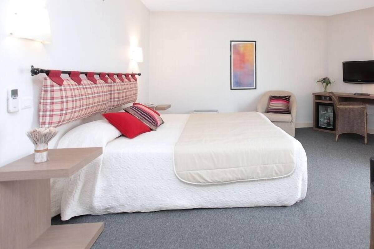 A hotel room with a bed, a desk, a chair, a TV, and a window with curtains.