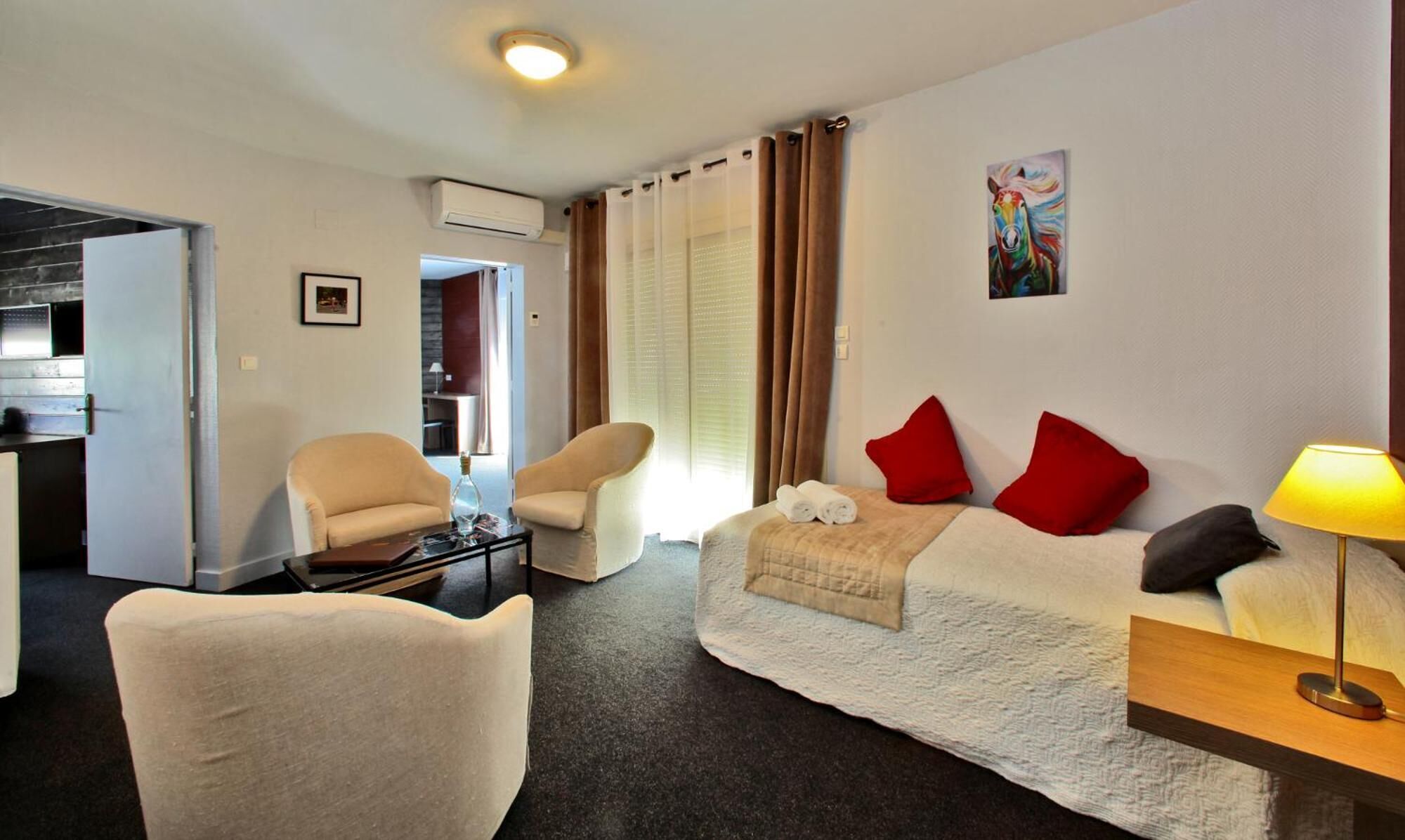 Een hotelkamer met een bed, twee stoelen, een tafeltje, een lamp en een schilderij aan de muur.