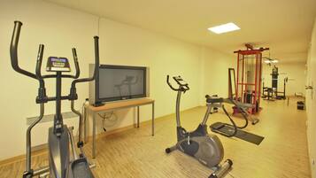 Ein Fitnessraum mit Ergometer, Crosstrainer, Fernseher und Kraftmaschine.