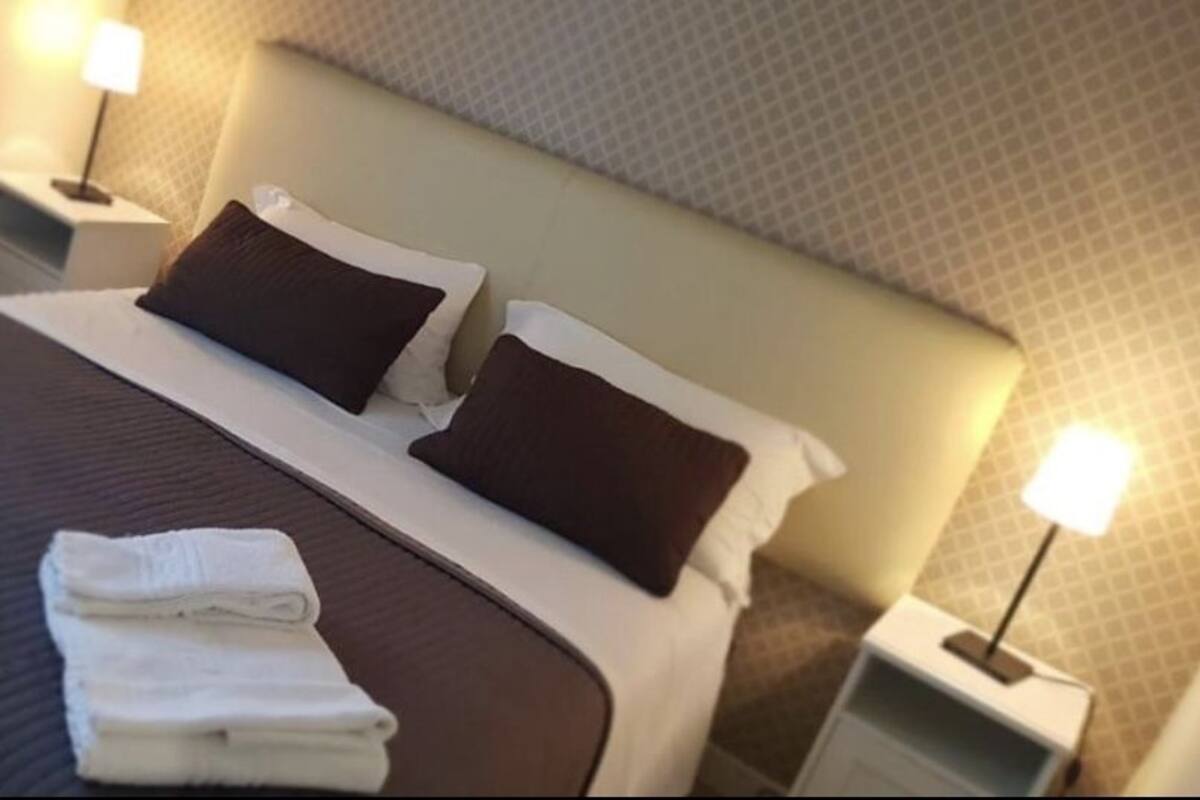Una cama bien hecha con dos almohadas, una toalla blanca doblada y una mesita de noche con una lámpara.