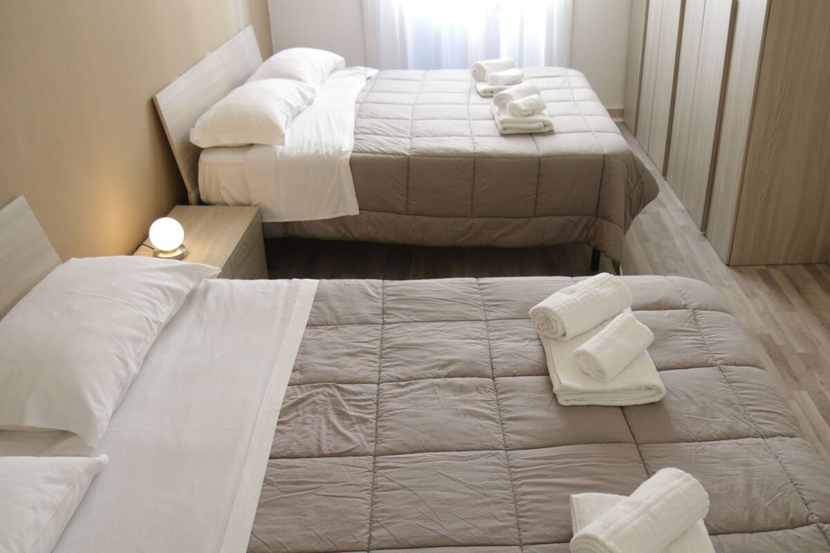 Habitación de hotel con dos camas, cada una con una colcha beige acolchada y almohadas blancas. Toallas bien dobladas sobre las camas.