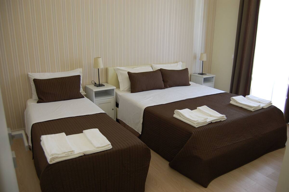 Habitación de hotel con dos camas individuales y una cama doble, cada una con toallas blancas bien dobladas.