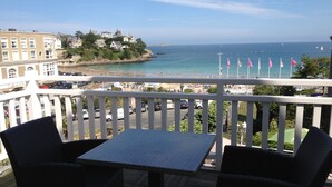 A balcony with two wicker chairs and a table, overlooking a beach with people and flags. - Hotel de la Plage (Dinard)