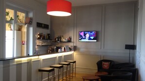 A bar area with stools, a television mounted on the wall, and a red hanging light fixture. - Hotel de la Plage (Dinard)