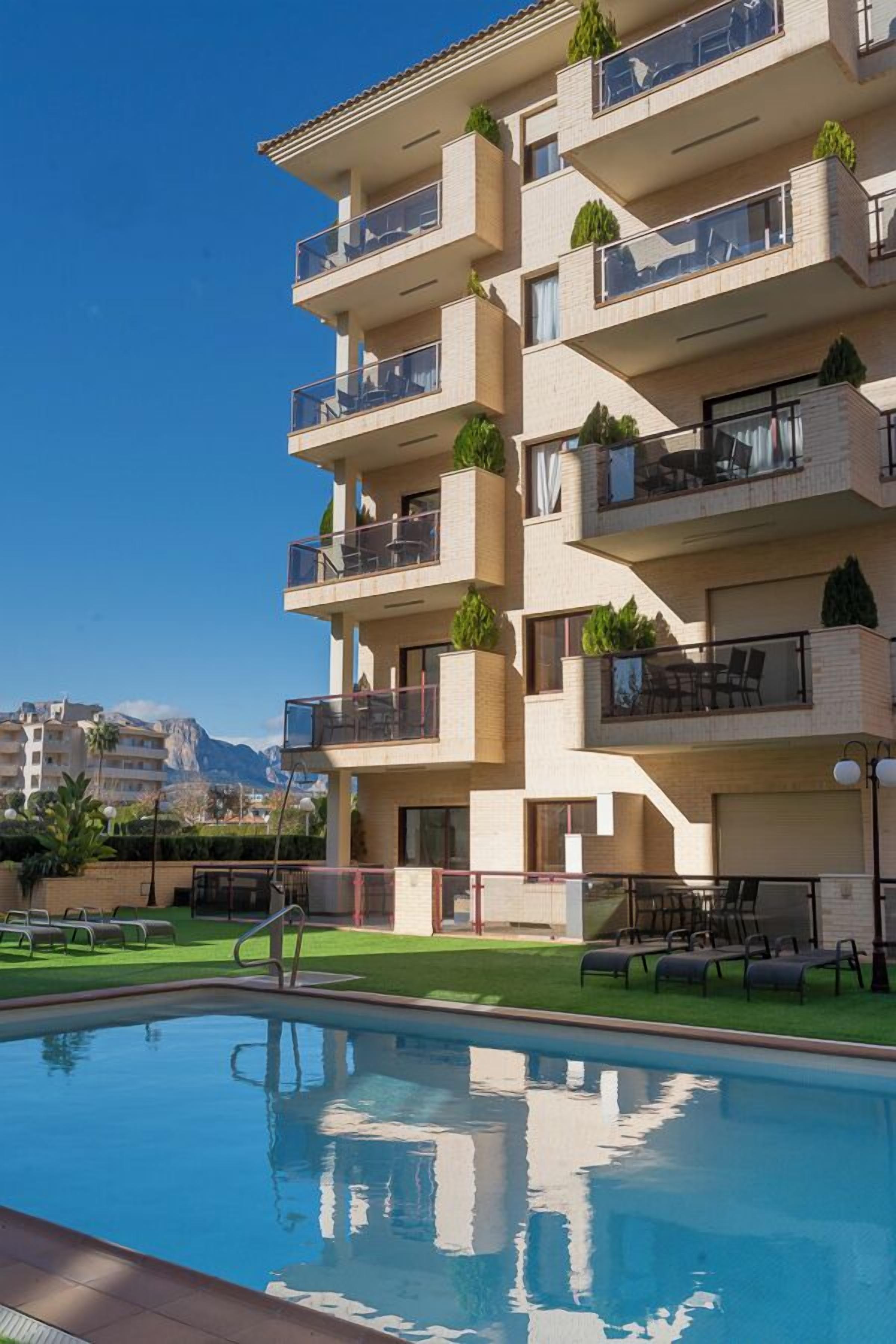 Un hotel a più piani con balconi, una piscina e vista sulle montagne.