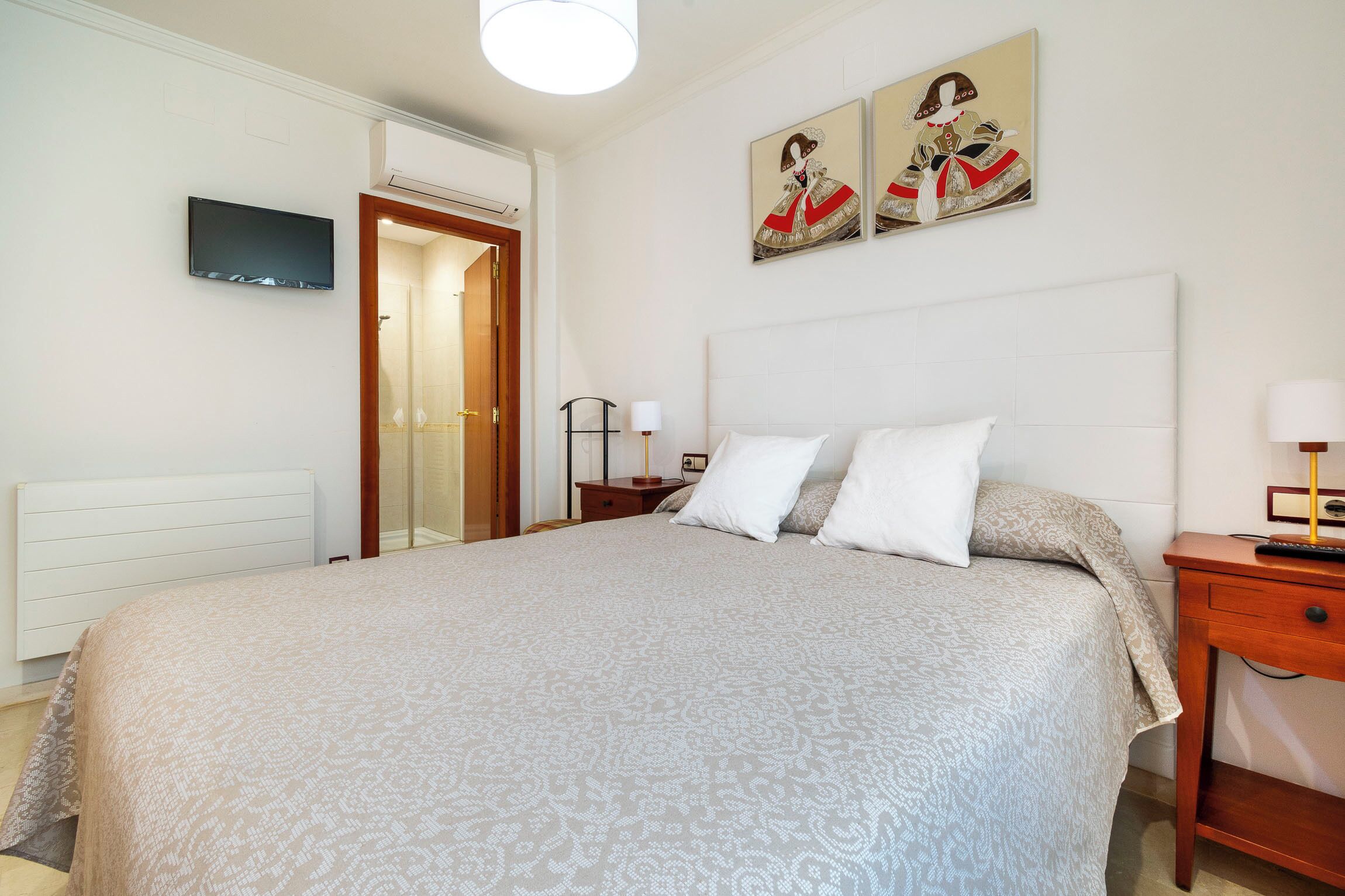Ein ordentlich eingerichtetes Schlafzimmer mit einem großen Bett, einem Nachttisch mit Lampe und einem an der Wand montierten Fernseher.
