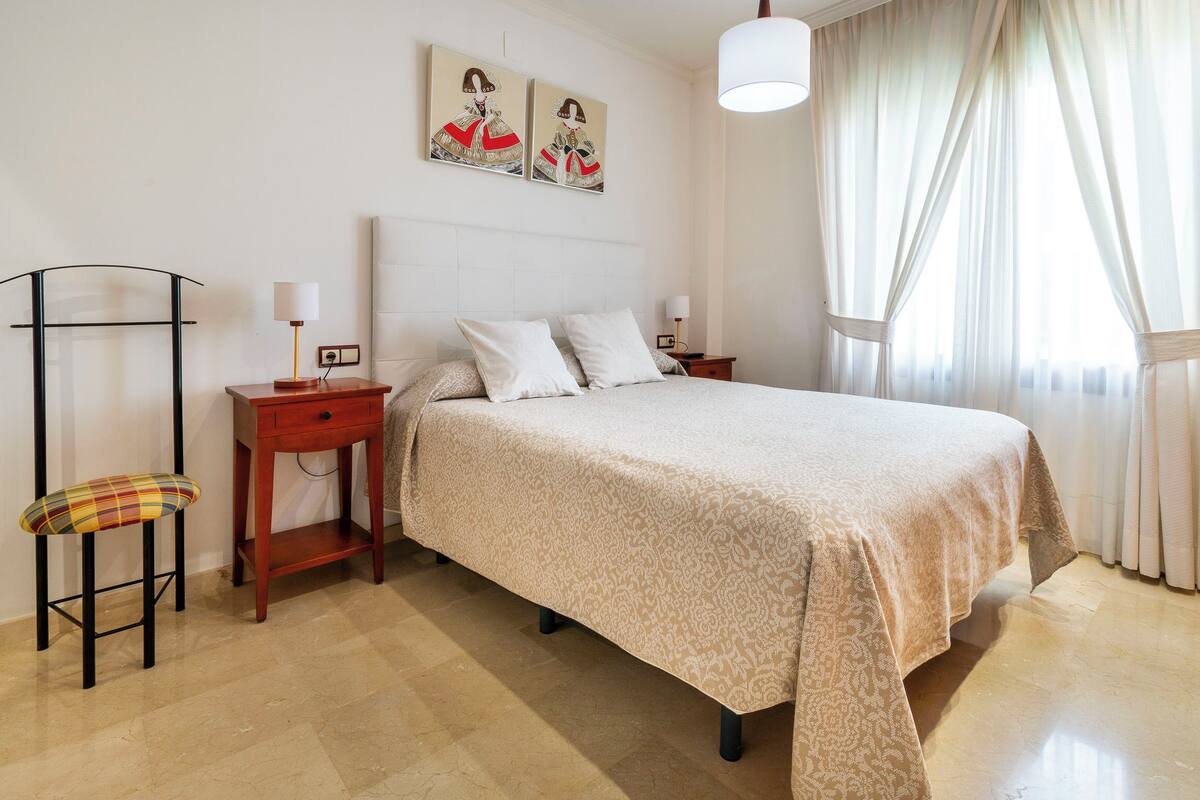 A neatly arranged bedroom with a large bed, bedside tables, a chair, and artwork on the wall.