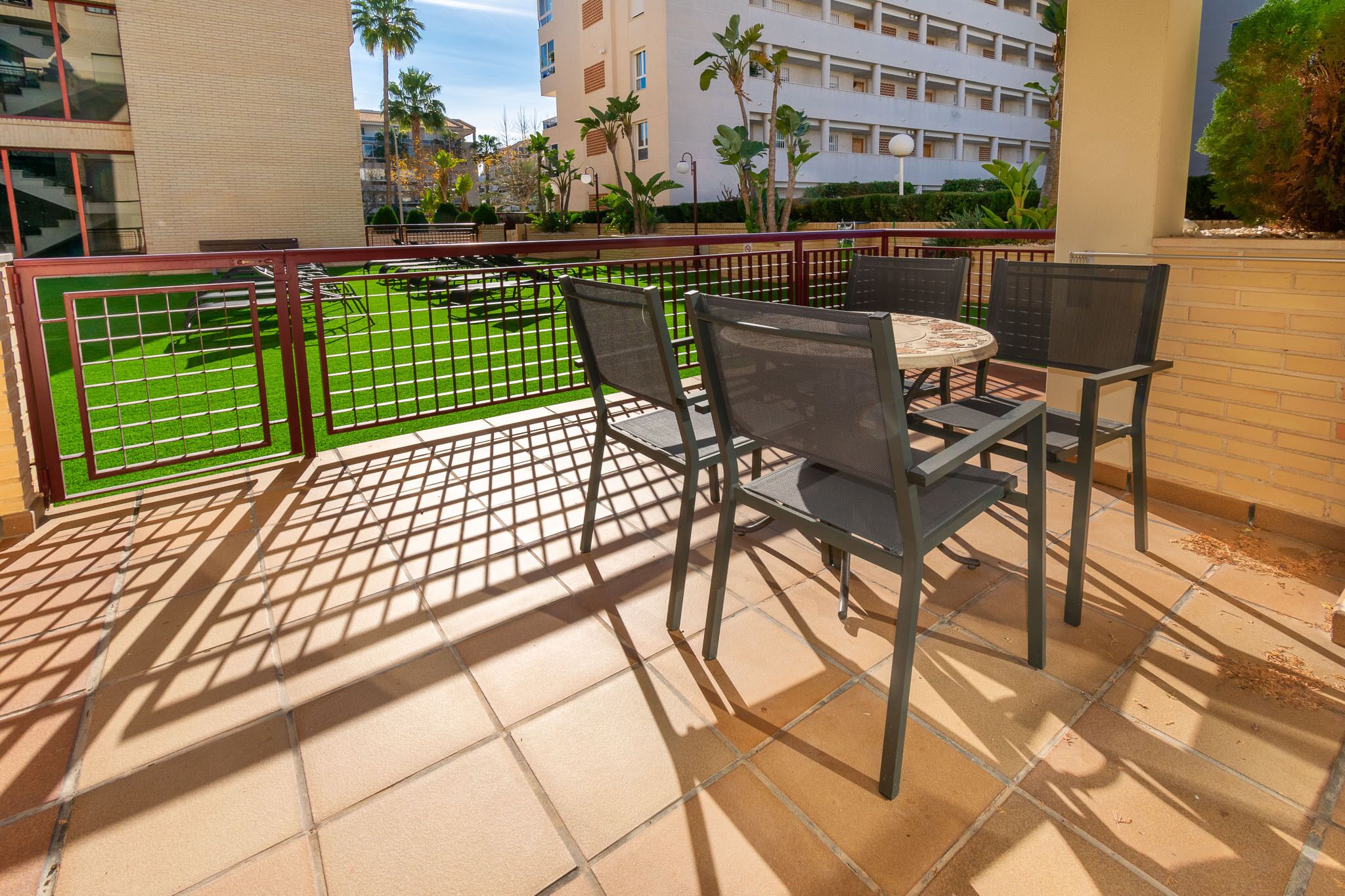 An outdoor patio with a table and chairs, a green lawn, and a building in the background.