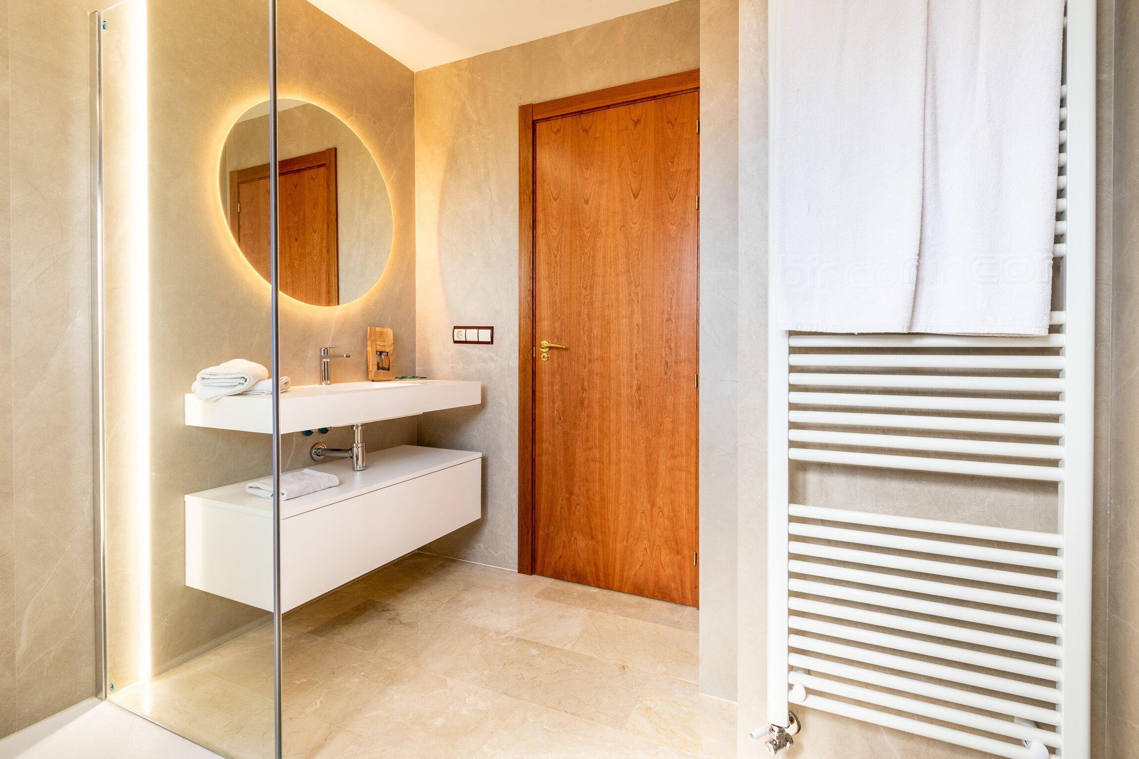 Een moderne badkamer met een glazen douchecabine, een houten deur en een witte handdoekhouder.