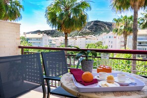 A balcony with a table set for breakfast, including a tray with orange juice, muffins, and a cup. There is a chair and a potted plant. - apartamentos Albir Confort (L'Alfas del Pi)