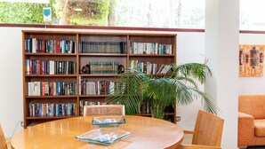 A library with bookshelves, a round table, chairs, and a potted plant. - apartamentos Albir Confort (L'Alfas del Pi)