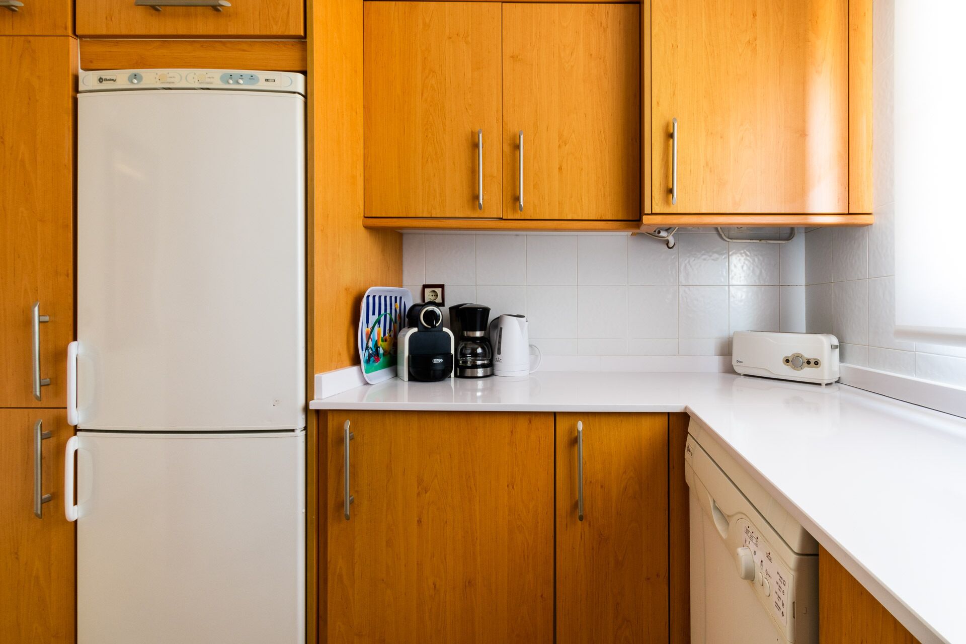 Una cocina con armarios de madera, un refrigerador blanco, una cafetera, un tostador y un lavavajillas.