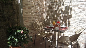 A patio with a stone wall, wicker chairs, a table set with breakfast items, and a potted plant. - Le Céretan Hôtel (Ceret)