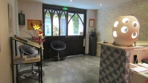 A reception area with a reception desk, a chair, a plant, and a wall with a geometric pattern. - Le Céretan Hôtel (Ceret)