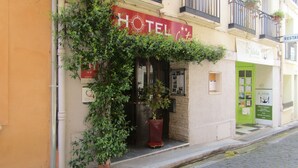 A hotel with a red sign, a green door, and a potted plant in front. - Le Céretan Hôtel (Ceret)