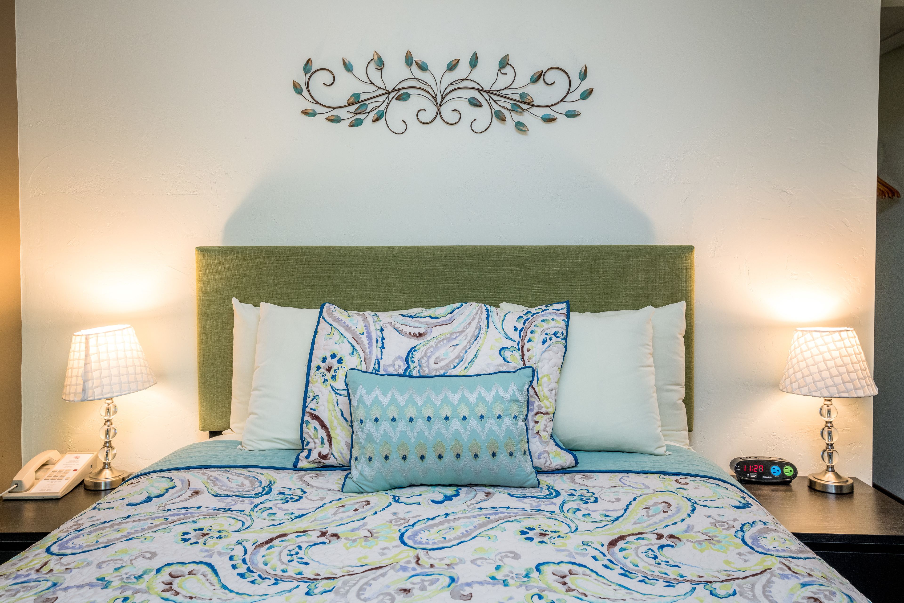 A neatly made bed with patterned bedding, two bedside lamps, a decorative wall piece, and a bedside clock.