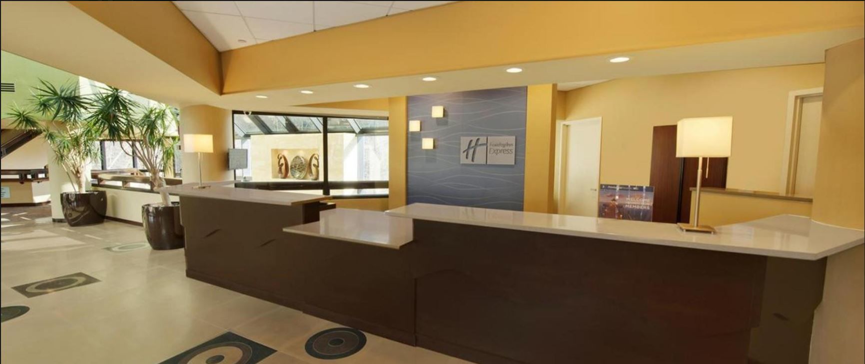 Un espace d’accueil d’hôtel au design moderne, comprenant un comptoir d’accueil, un coin salon et une vue sur le hall d’entrée.