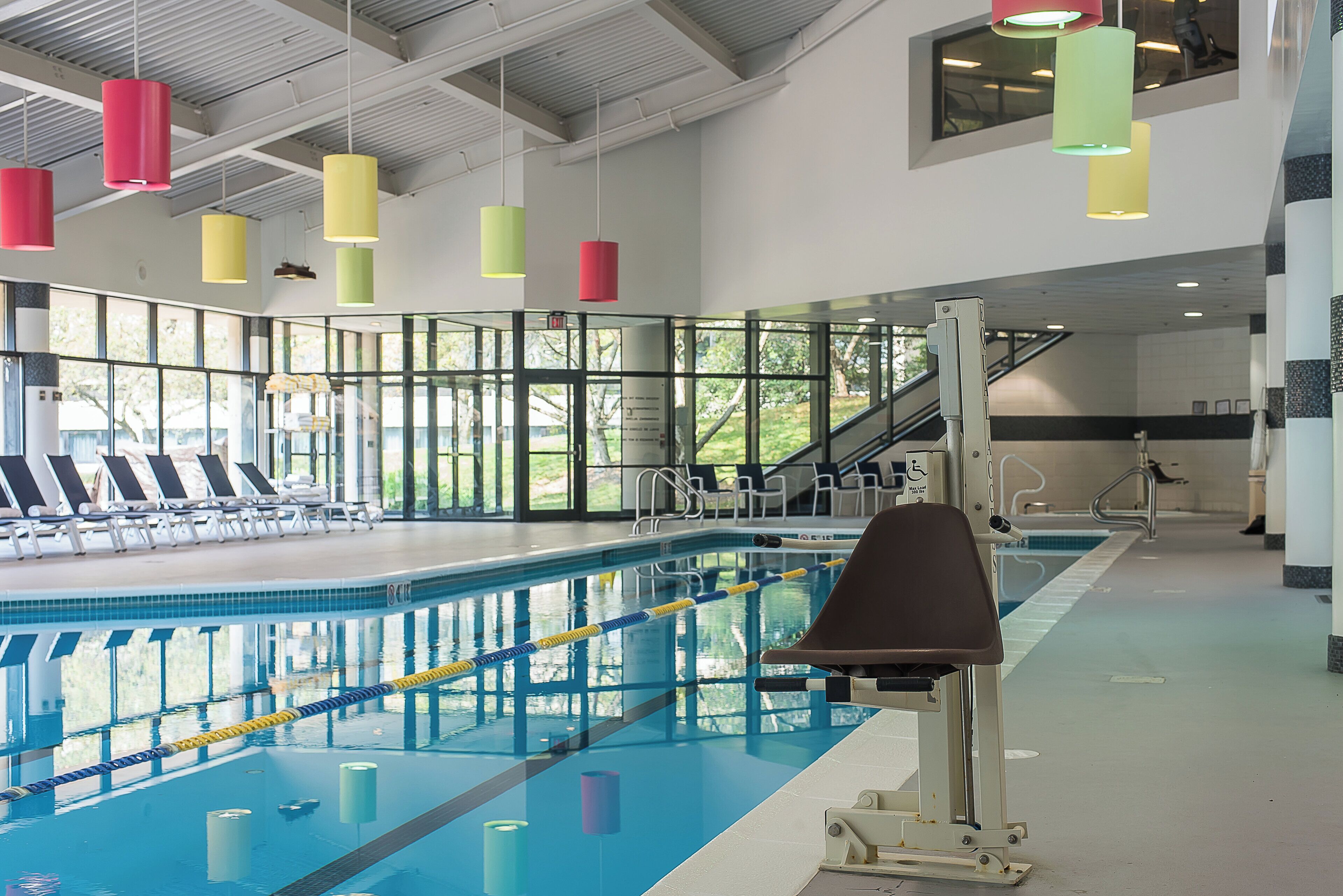 A swimming pool with clear lanes, a lifeguard chair, and a glass wall with a view of the outdoors.